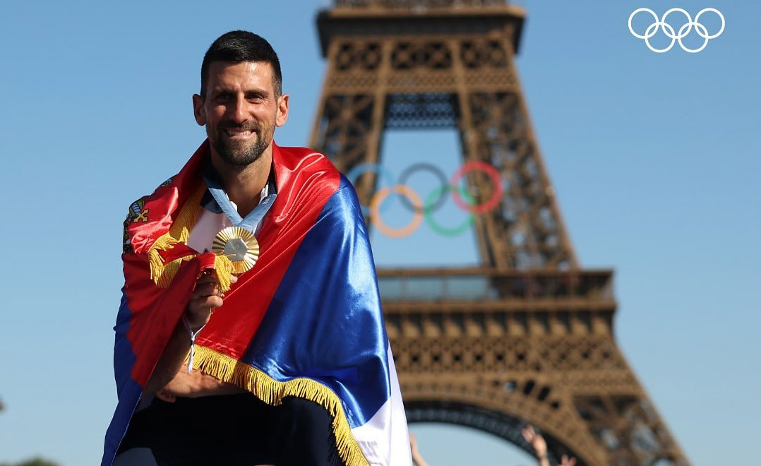 Novak Djokovic wearing a Serbian flag and holding his gold medal in front of the Eiffel Tower.